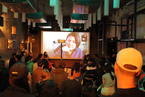 A group of people watching a large projection screen with a woman looking pleased to be there.